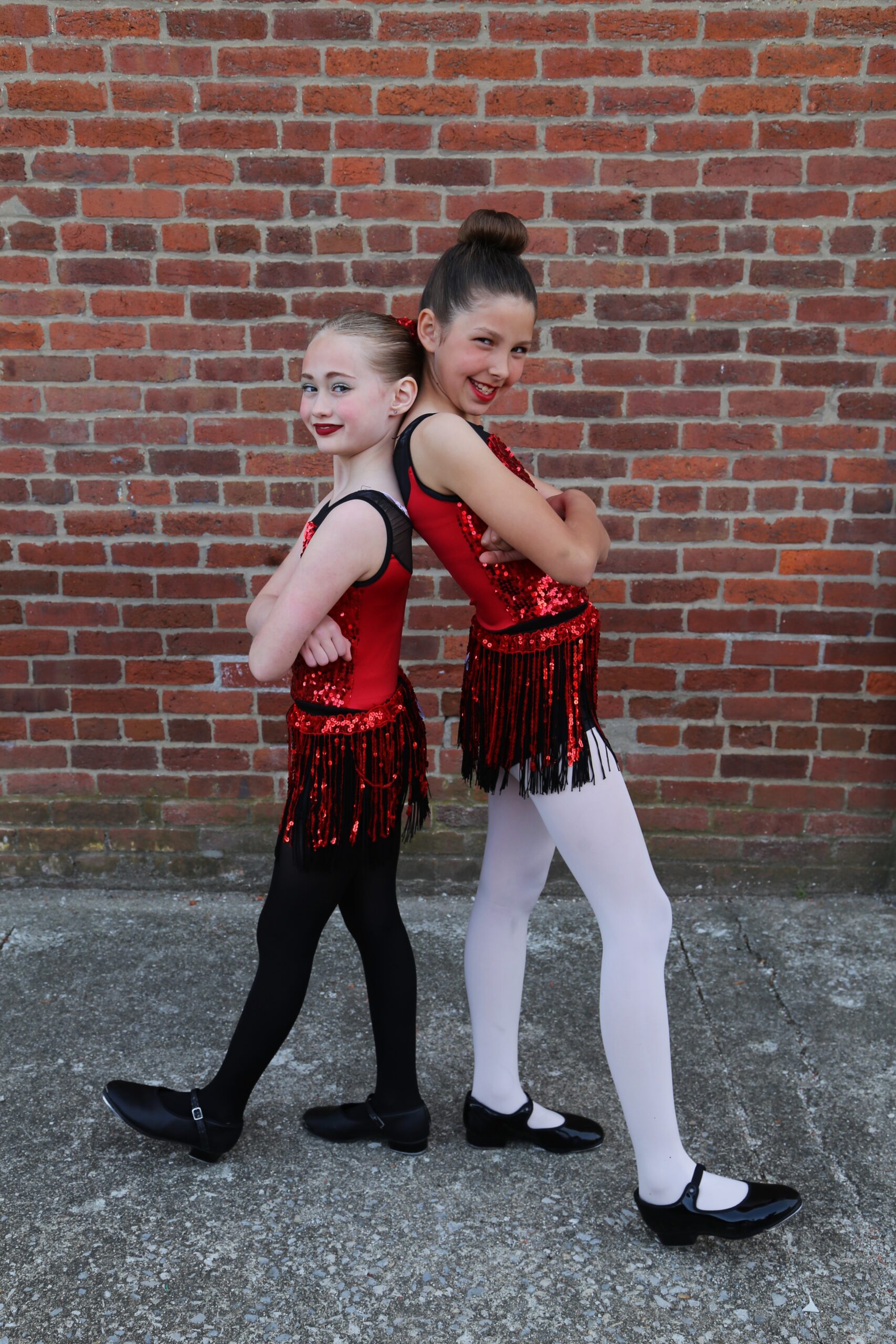 All That Jazz duo posing against a brick wall in red and black outfits