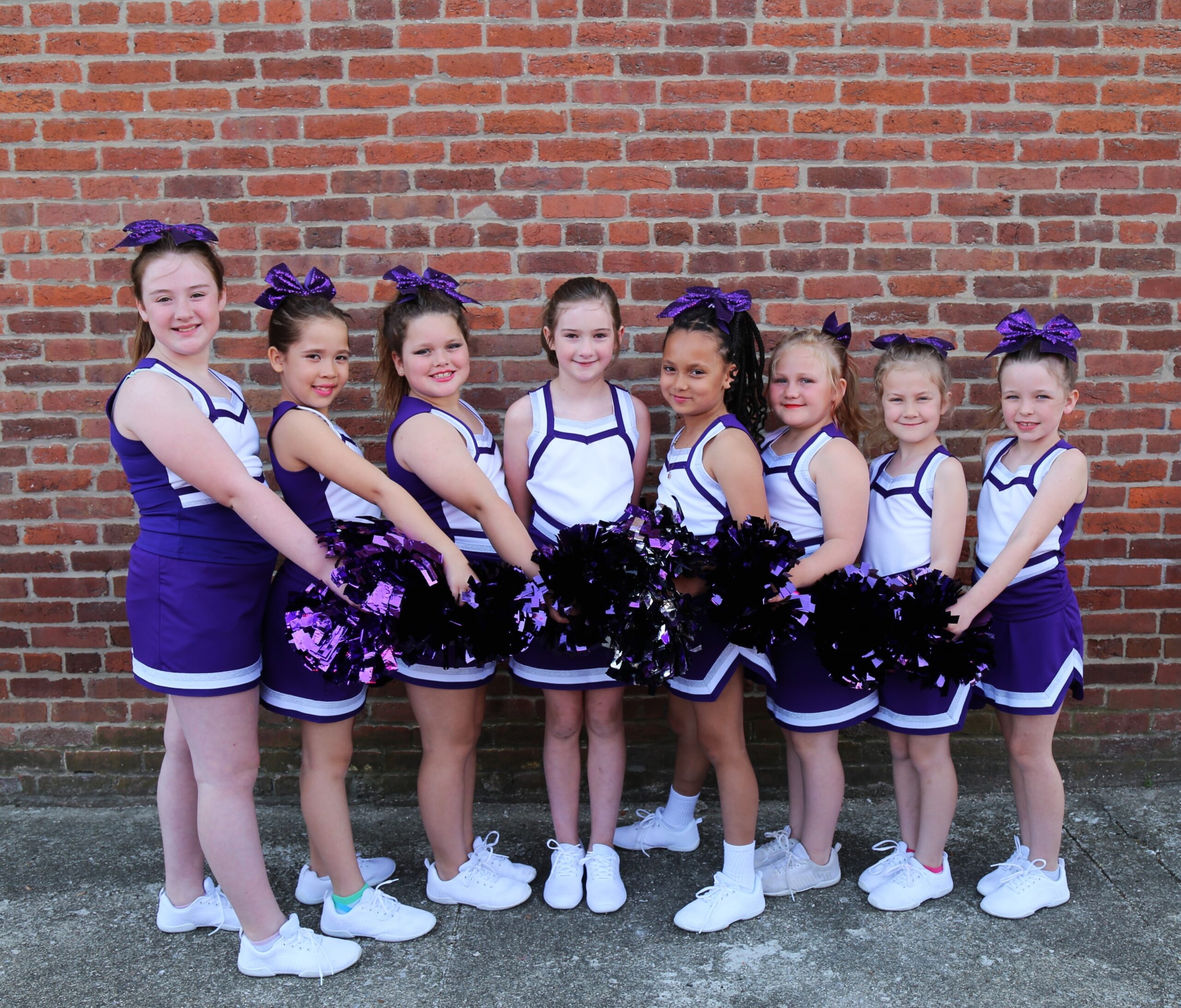 Dynamite Tumblers cheerleading group posing against a brick wall in purple and white uniforms