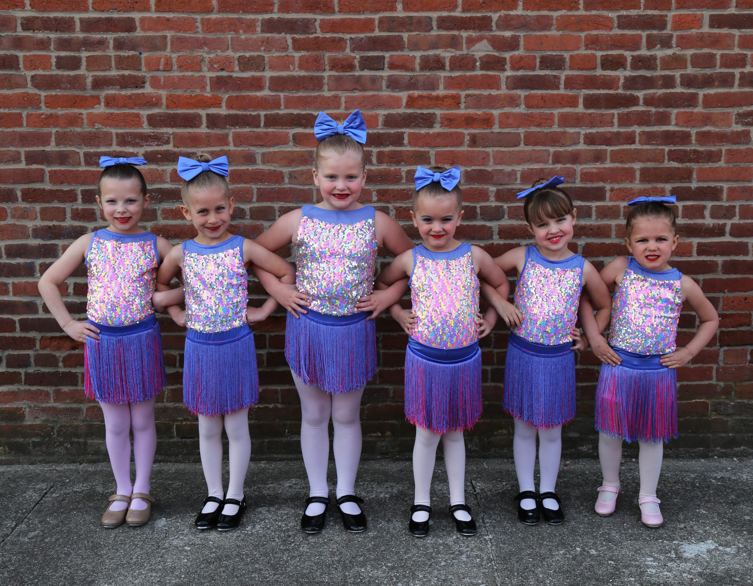 Tutus & Tap group posing in sparkly outfits against a brick wall