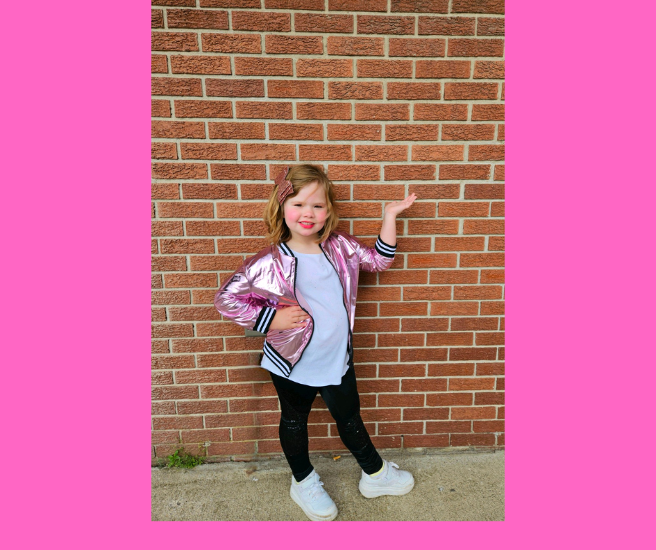 Zumba Kids dancer posing against a brick wall in a shiny pink jacket